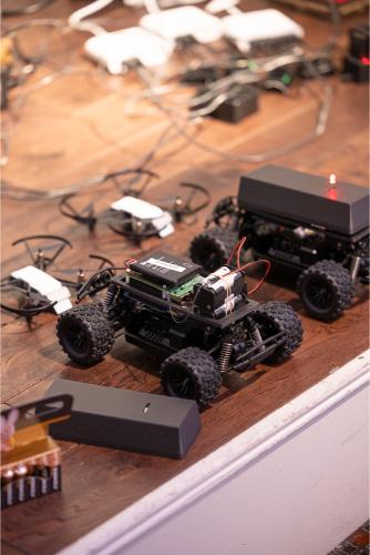Small wheeled robots and radio kit laid out on a workbench during a hardware workshop.