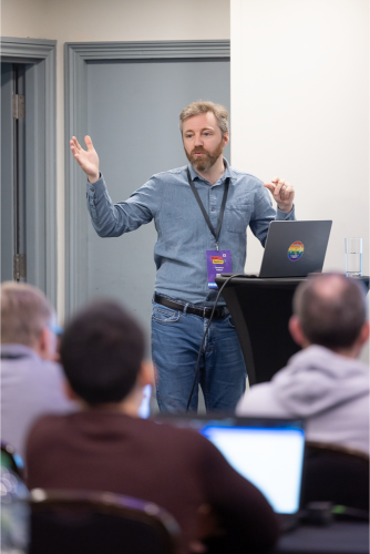 A speaker mid gesture presenting to a seated workshop room.