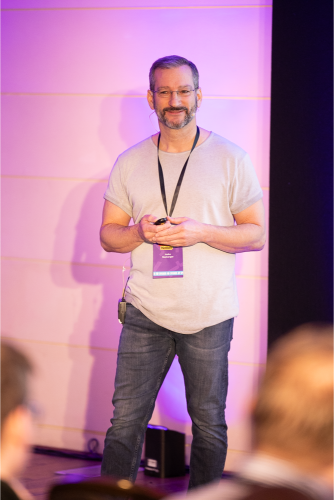 A speaker standing on stage in front of a lit backdrop.